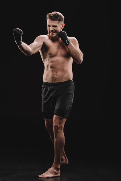 tense muscular barefoot mma fighter in bandages doing punch on black