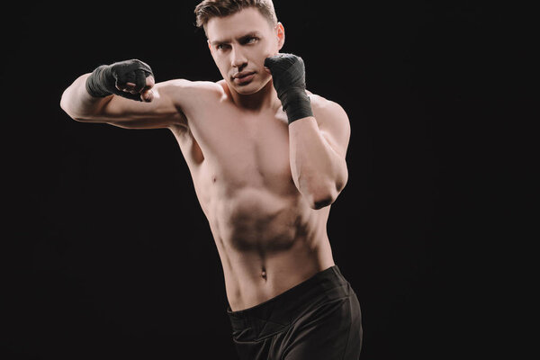 сильный атлетический мускулистый спортсмен в бинтах делает пунш изолированный на черном
