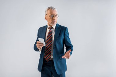 akıllı telefon ve mimik gri izole tutan takım elbiseli olgun iş adamı 