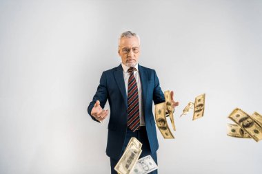 selective focus of mature businessman in glasses throwing in air dollar banknotes isolated on grey  clipart