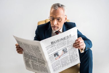 mature businessman in glasses and suit reading business newspaper isolated on grey clipart