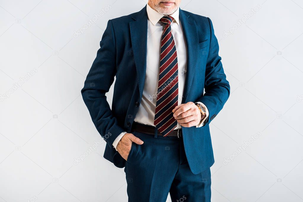 cropped view of mature businessman in suit standing with hand in pocket isolated on grey