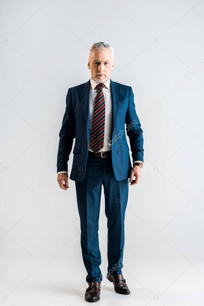 serious middle aged businessman in suit standing on grey  