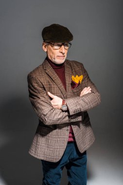 trendy orta yaşlı adam gözlük ve Grey çapraz kollar ile ayakta kap 