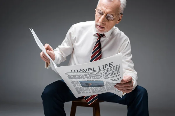 mature businessman in glasses reading travel newspaper on grey