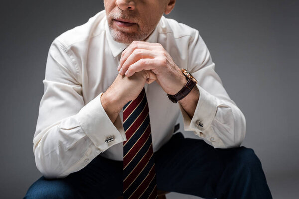 обрезанный вид зрелого бизнесмена с сжатыми руками на сером
 