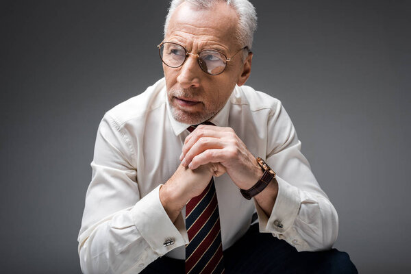 вдумчивый зрелый бизнесмен с сжатыми руками на сером
 