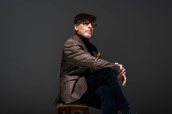 low angle view of stylish mature man in cap and glasses on grey