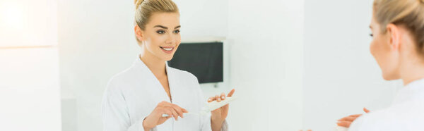 панорамный снимок красивой женщины, наносящей зубную пасту на зубную щетку
 