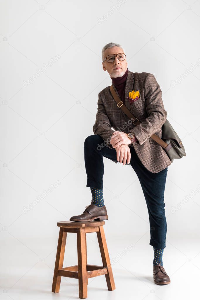 fashionable mature man putting leg on chair while standing on grey 