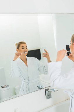 diş fırçalama ve selfie alarak beyaz bornoz içinde kadın seçici odak