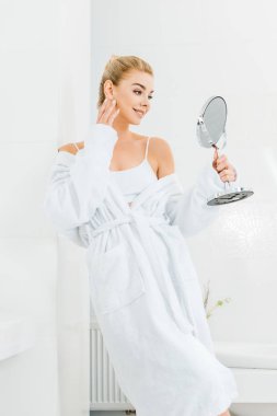 beyaz bornoz banyo aynaya bakarak çekici ve gülümseyen kadın 