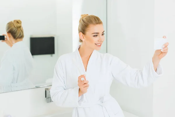 选择焦点的美丽的女人在白色浴衣拿着牙刷和在浴室自拍自拍 — 图库照片