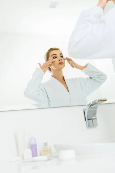 白いバスローブ バスルームでの顔のクリームを適用することで魅力的な女性の選択と集中 — ストック写真