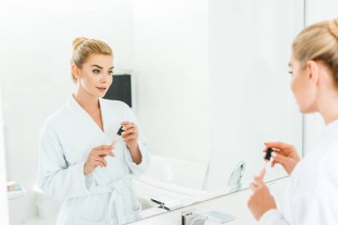 seçici odak içinde dudak parlatıcısı banyoda holding beyaz bornoz güzel kadın