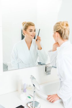 seçici odak kozmetik fırça banyoda holding beyaz bornoz içinde kadın 