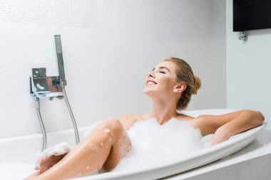 çekici, sarışın ve gülümseyen kadın alarak banyo banyoda köpüklü 