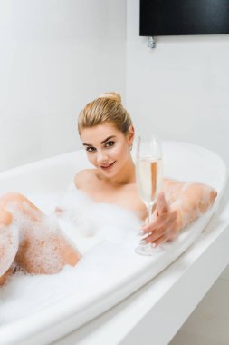 banyo ve şampanya kadehi banyoda tutan güzel ve gülümseyen kadın seçici odak 