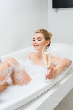 Şampanya cam banyo güzel ve gülümseyen kadın tarafından tutarak seçici odak 