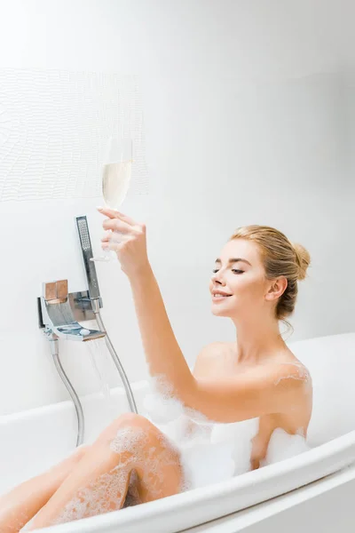 バスルームのガラスの魅力的な笑みを浮かべて女性入浴と保持シャンパン — ストック写真
