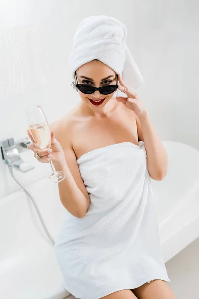 サングラス タオル シャンパン グラスを持って バスルームでカメラ目線で美しく 笑顔の女性 — ストック写真