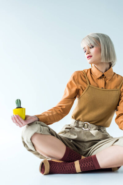 beautiful stylish girl sitting and holding cactus plant isolated on white