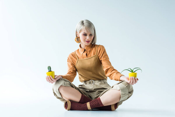 beautiful stylish girl sitting and holding flower pots on white