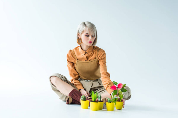 beautiful stylish blonde girl sitting with flower pots on white 