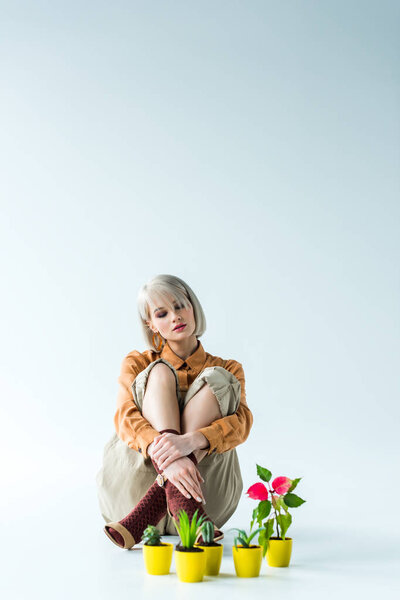 красивая стильная блондинка сидит возле цветочных горшков на белом с копировальным пространством
