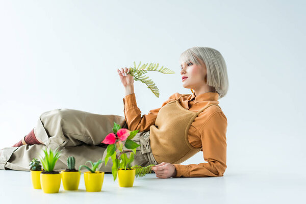 beautiful stylish girl holding fern leaves while posing near flower pots isolated on white