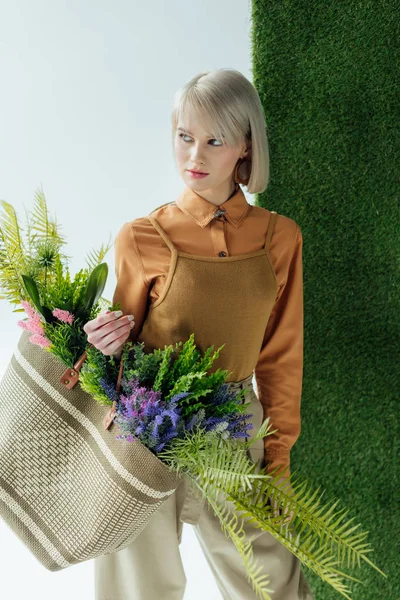 美丽的时尚女孩举行袋与蕨类植物和鲜花在白色与绿草 — 图库照片