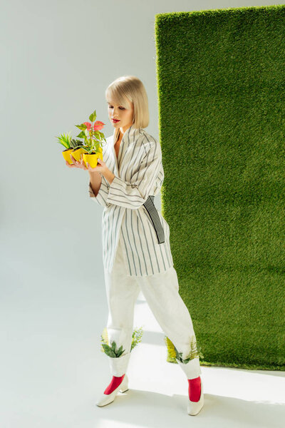 beautiful stylish girl holding flower pots on grey with green grass 