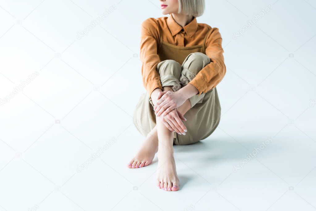 cropped view of stylish young woman sitting with crossed legs on white