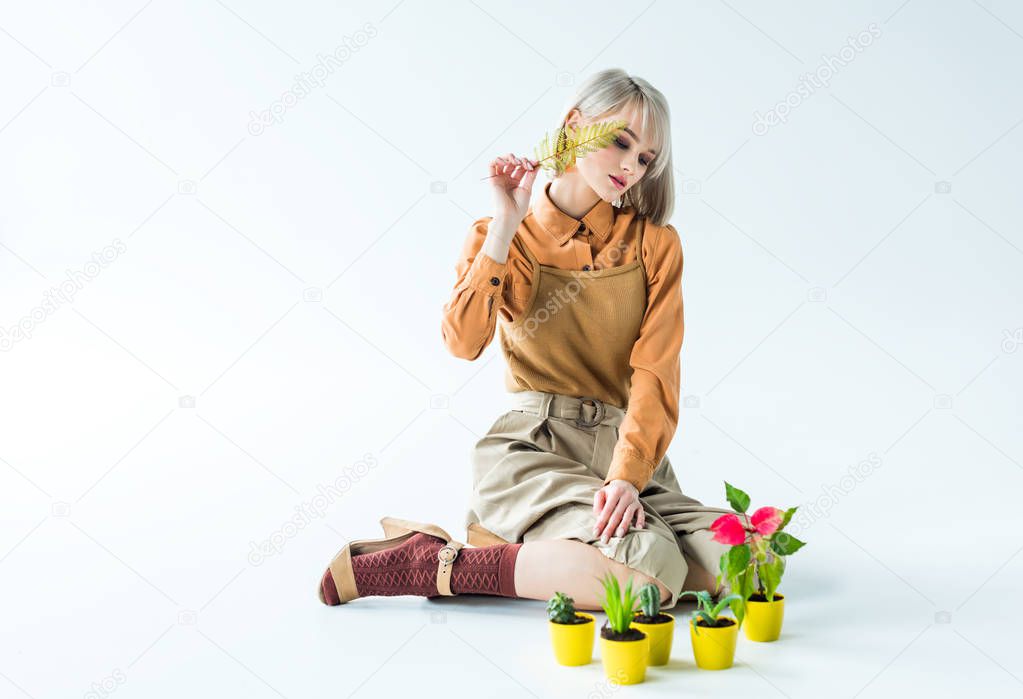 beautiful stylish girl sitting and posing with fern leaf and flower pots on white