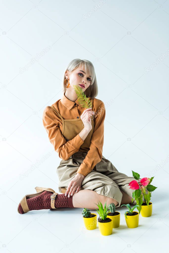 beautiful stylish girl posing with fern leaf near flower pots on white