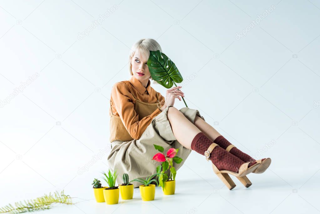 beautiful stylish girl posing with green leaf near flower pots on white 