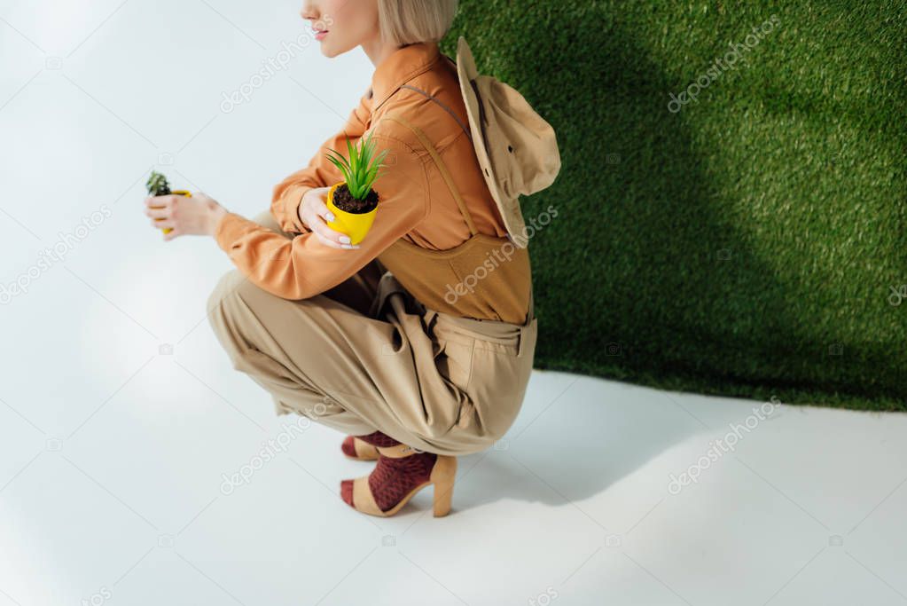 partial view of stylish girl holding flower pots on grey with green grass 