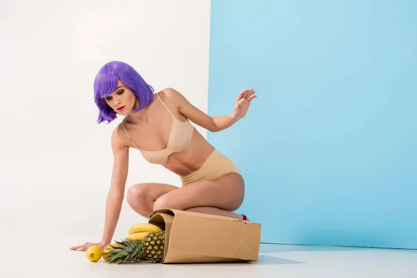 美丽的女孩与紫色的头发摆近纸袋与热带水果在蓝色和白色与复制空间 — 图库照片