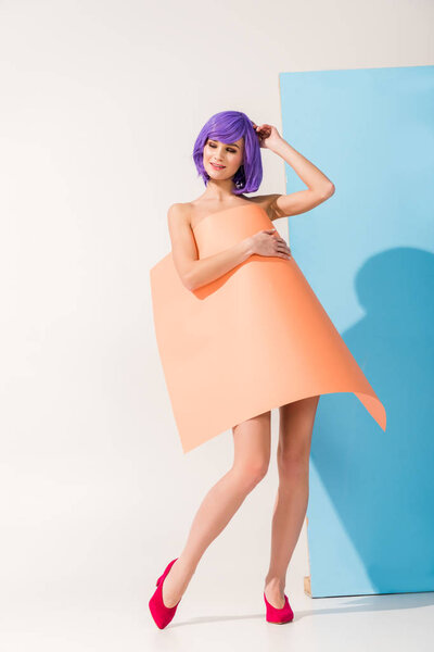 beautiful smiling girl with purple hair covered in coral paper sheet posing on blue and white