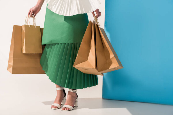 cropped view of stylish girl in paper clothes with shopping bags on blue and white
