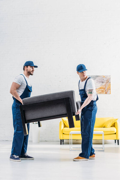two movers in uniform transporting furniture in apartment with copy space