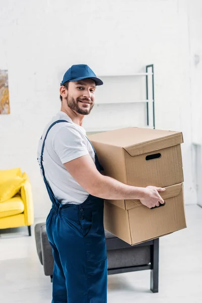 Knappe Verhuizer Uniform Kijken Naar Camera Terwijl Uitvoering Kartonnen Dozen — Stockfoto