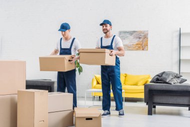 two movers transporting cardboard boxes in apartment clipart