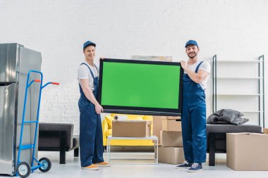 dairede yeşil ekran ile TV taşıırken üniformalı iki taşıyıcılar kamera bakıyor