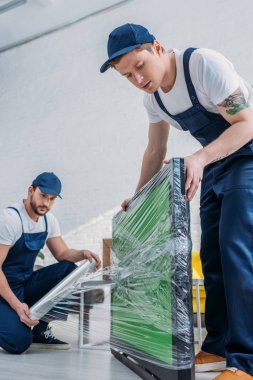 dairede yeşil ekran ile tv sarma sırasında streç film rulo kullanarak üniforma iki yakışıklı movers