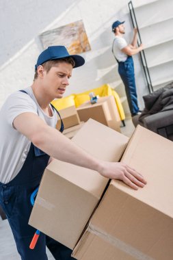 two movers transporting cardboard boxes and furniture in apartment clipart