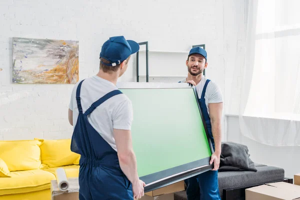 two movers in uniform transporting tv with green screen in living room