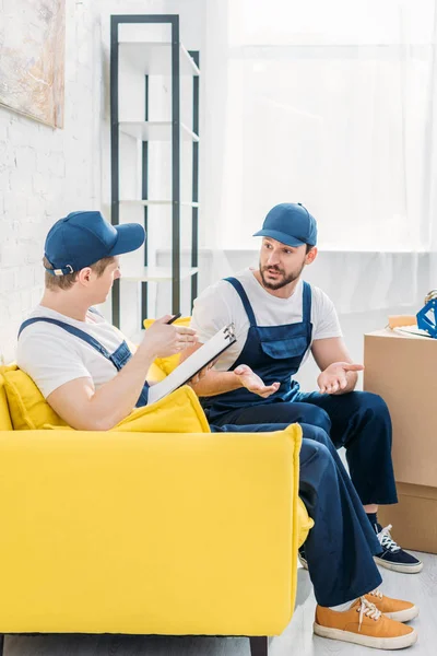 Two Movers Writing Clipboard Gesturing Hands While Sitting Sofa Apartment — Stock Photo, Image