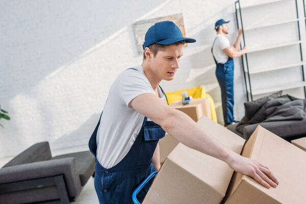 two movers transporting cardboard boxes and furniture in apartment with copy space