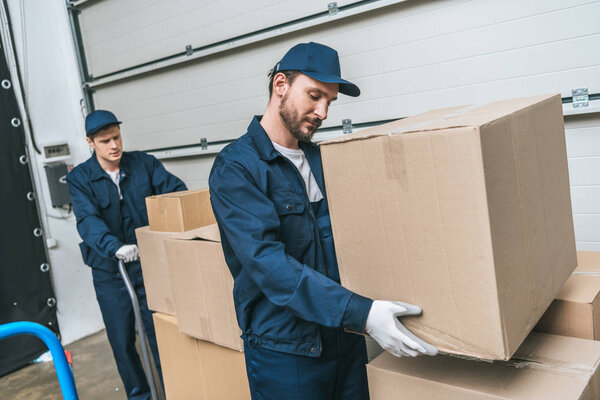 two concentrated movers in uniform transporting cardboard boxes in warehouse